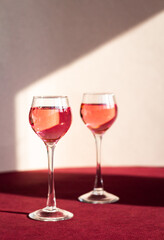 two glasses with pink gin, berry liqueur or any red alcoholic drink, light and shadow on the background, minimalism, copy space
