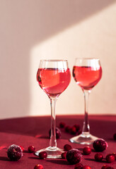Fototapeta na wymiar two glasses with pink gin infused with cranberry, light and shadow on the background, berry liqueur or red alcoholic cocktail