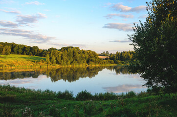 Summer serene landscape with calm river and green hills at sunrise.