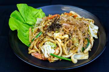 Stir-fried seafood udon noodles with squid and shrimp on a plate.