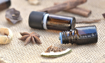 bottles of essential oil with  stick of cinnamon, badian  and dried fruit with shell   on a natural fabric background