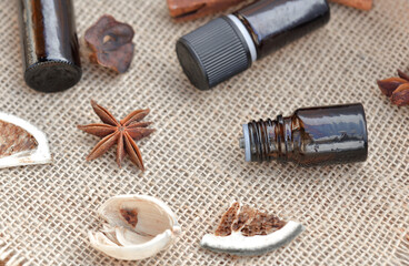 bottles of essential oil with; stick of cinnamon; badian; and dried fruit with shell; on a natural fabric background