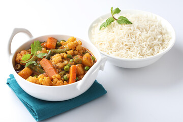 MIX VEGETABLE CURRY WITH RICE - indian recipe, mixed veg containing Carrots, cauliflower, green peas and beans with traditional masala and curry, red hot and spicy served in a ceramic bowl
