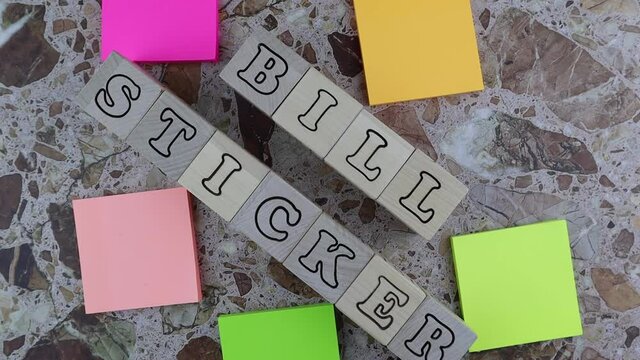 Biller Sticker concept with brightly colored memo pads forming a frame around wooden cubes with alphabet letters viewed top down on marbled stone. Rotating table