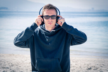 man with sunglasses and headphones listening to music on the beach