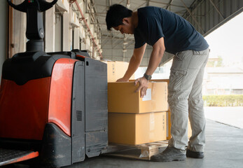 Asian Warehouse Worker Lifting Card Board Boxes on Pallet. Warehouse. Storage. Cargo Shipment Boxes.