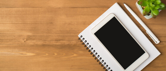 Top view photo of workplace with pen plant and smartphone display on copybook isolated wooden table background with copyspace