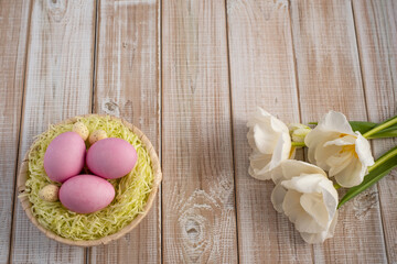 Easter eggs in a nest on a wooden background with white tulips