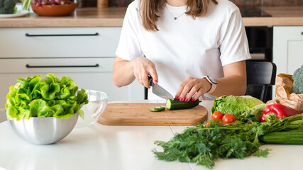 Brunette Woman in white t-shirt preparing vegetable salad in the kitchen at home, Wife Cutting ingredients on table. Healthy Food, Vegan Salad. Dieting Concept.