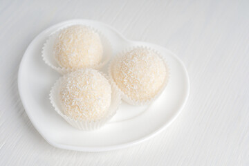 Fototapeta na wymiar Coconut organic sweet truffles or homemade nut vegetarian energy balls served in heart shaped plate on white wooden background at kitchen ready to eating for breakfast. Horizontal orientation image