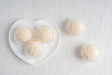 Top view of coconut organic truffles dessert or homemade nut vegan energy balls served in heart shaped plate on white wooden background at kitchen ready to eating for breakfast. Horizontal image