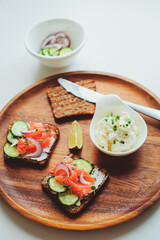 tasty diet food for breakfast or brunch - avocado and salmon toast with cream cheese, cucumber and red onion served on wooden plate