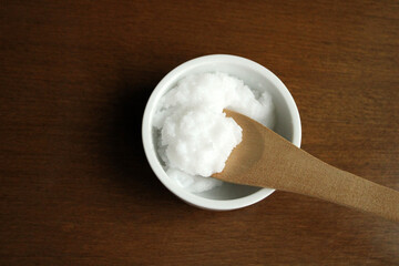 Natural coconut oil in the bowl, top view, wooden background