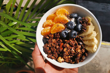 Bowl of homemade granola with yogurt and fresh berries, banana and mandarin orange from top view