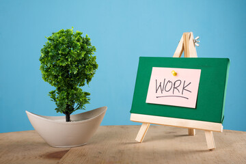 Work written on a sticky note on a mini green notice board with a plant with blue background.