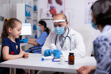 Professional therapeutist choosing drugs for medical disease. Specialist in treatment illness wearing protection mask and visor against coronavirus providing healtcare services during global pandemic