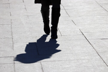 Silhouette and shadow of lonely woman in boots walking on a street. Concept of loneliness, female fashion in early spring