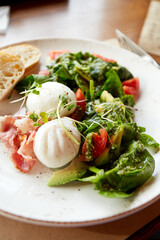 Healthy breakfast. Poached eggs, Steak Salad with bacon, arugula, tomato and avocado. Morning sunlight
