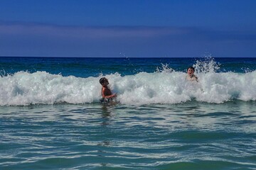Naklejka premium Niños saltando olas en la playa