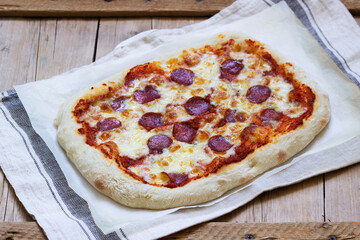 Homemade pizza with tomato sauce, herbs, sausage and cheese on a wooden table.