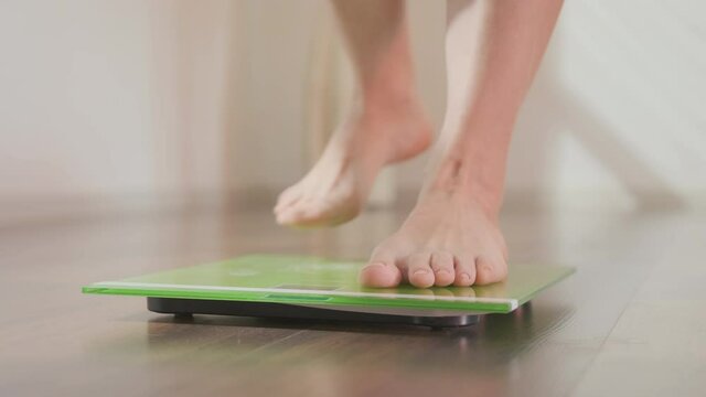 Women's Feet Step On Floor Scales Close Up. Woman Measuring Her Body Weight By Standing On Electronic Scale Indoors.