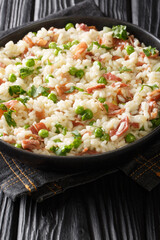 Risi e Bisi classic Italian comfort food of rice with peas and chunks of ham close up in a plate on the table. Vertical