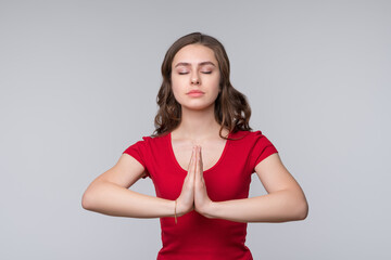 Attractive brunette girl prays for wellness of family, keeps palms pressed together in praying gesture, saying namaste