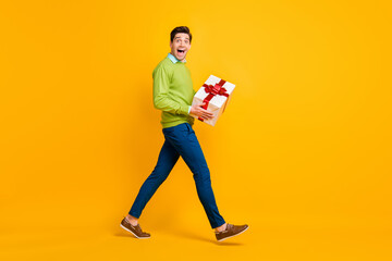 Full length body size profile side view of nice crazy cheerful guy holding in hands giftbox having fun isolated on bright yellow color background