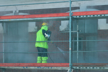 A worker washes the wall of a building with a high pressure water jet. Scaffolding. Scaffolding.