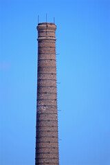 The top of an old red brick chimney against a blue sky