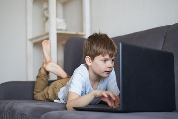 Boy sitting at home on the sofa and holding a laptop in his hands, gadget addiction concept, virtual online learning