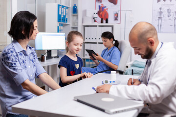 Fototapeta premium Doctor in white coat writing treatment during medical examination in clinic office. Caring pediatrician discussing symptoms against disease with mother in medical hospital