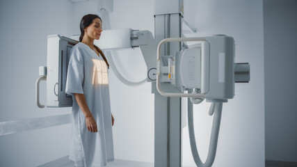 Hospital Radiology Room: Beautiful Multiethnic Woman Standing in Medical Gown in the X-Ray Machine....