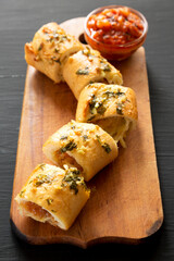 Homemade Chicken Parmesan-Stuffed Garlic Bread on a rustic wooden board on a black background, side view.