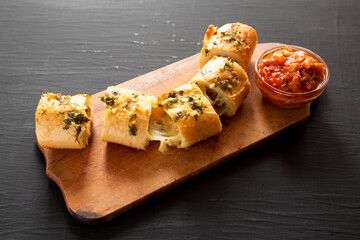 Homemade Chicken Parmesan-Stuffed Garlic Bread on a rustic wooden board on a black background, side view.