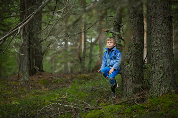 a 7-9-year-old boy in a blue denim jacket walks in the summer forest, selective focus