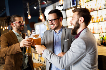 Happy young businessmen drinking beer and talking at pub after work