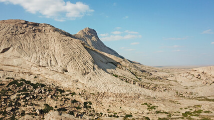 Huge rocks from lava. A former volcano. Bektau-ATA Tract. Large rocks, rifts, cracks, and mountains. In places, grass grows and water is visible. Unusual Martian landscape. Blue sky and clouds.