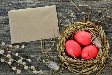 Easter decorative composition with bright pink painted eggs in a nest of straw with feathers on a dark background with envelope and willow twigs top view.