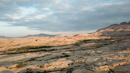 Dawn over frozen lava and mountains. Huge rocks and a gorge cast a shadow from the sun. Grass and...