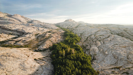 Dawn over frozen lava and mountains. Huge rocks and a gorge cast a shadow from the sun. Grass and...