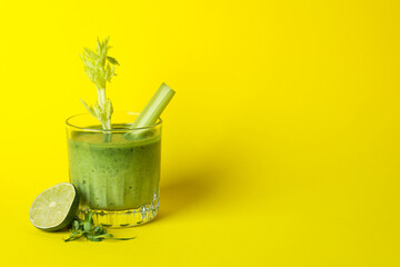 Glass of green smoothie and ingredients on yellow table