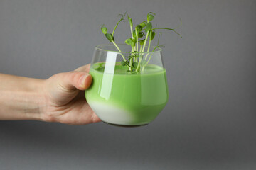 Female hand hold glass of green smoothie on light gray background