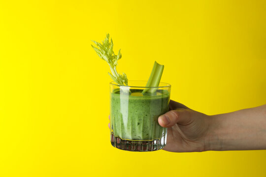 Female hand hold glass of smoothie on yellow background
