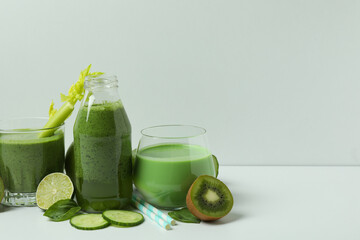 Glasses of green smoothie and ingredients on white table