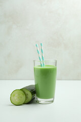 Glass of green smoothie and cucumber on white table