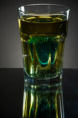 Premade setup for saint patrick drink. Shot glass of blue curacao drink inside the light gold beer. Reflecting surface and dark gradient background