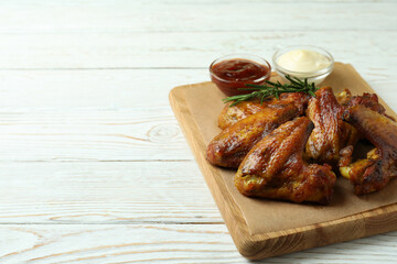 Concept of tasty food with baked chicken wings on white wooden background