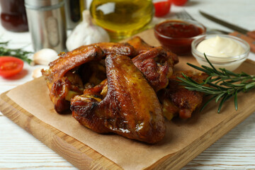 Concept of tasty food with baked chicken wings on white wooden background