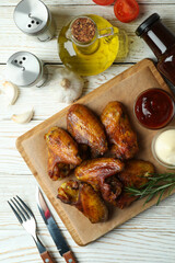 Concept of tasty food with baked chicken wings on white wooden background